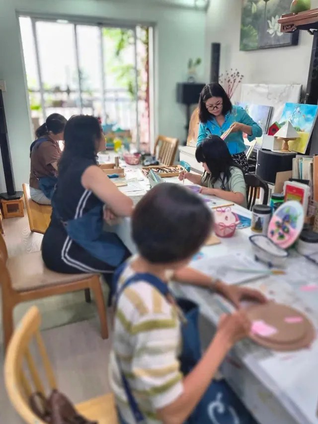 Học viên nhiều độ tuổi cùng vẽ và làm đồ thủ công quanh bàn lớn trong một buổi workshop