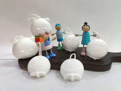 Xà phòng trắng hình mèo tròn có dây treo, bên cạnh đồ chơi gỗ
